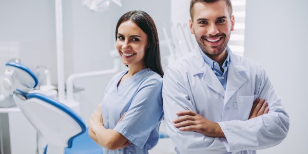 smiling doctor and assistant with crossed hands looking at the camera in dental clinic